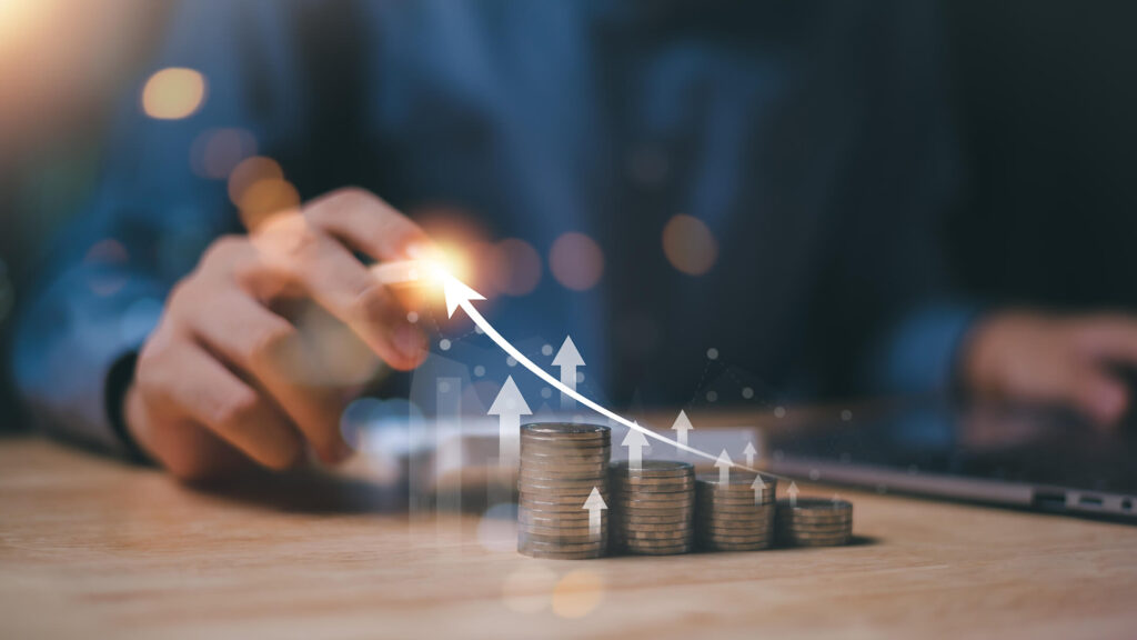Hand pointing at a stack of coins with an upward trend graph overlay, symbolizing financial growth and investment.